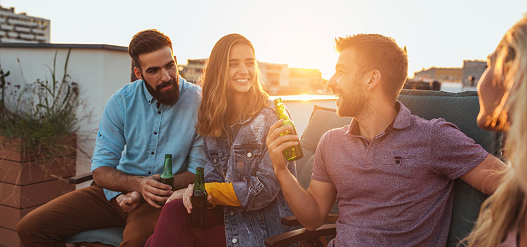 Four friends chat amiably on the rooftop of a bar as the sun sets behind them.