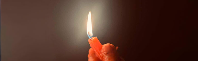 A lit candle drips wax down over the hand of the person holding it.